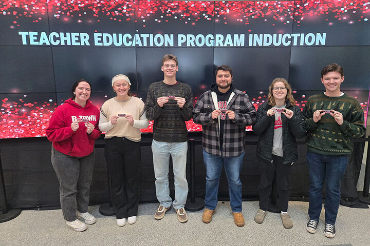 A group of students stands in front of a Teacher Education Program Induction sign.